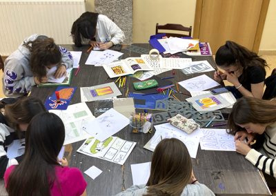 Foto-de-un-taller-de-estampación-con-niñas-trabajando-sobre-una-mesa-llena-de-papeles-y-material-de-diseño